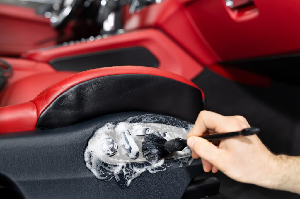 Cleaning the car interior with a brush. A car detailing worker cleaning the interior of a car.