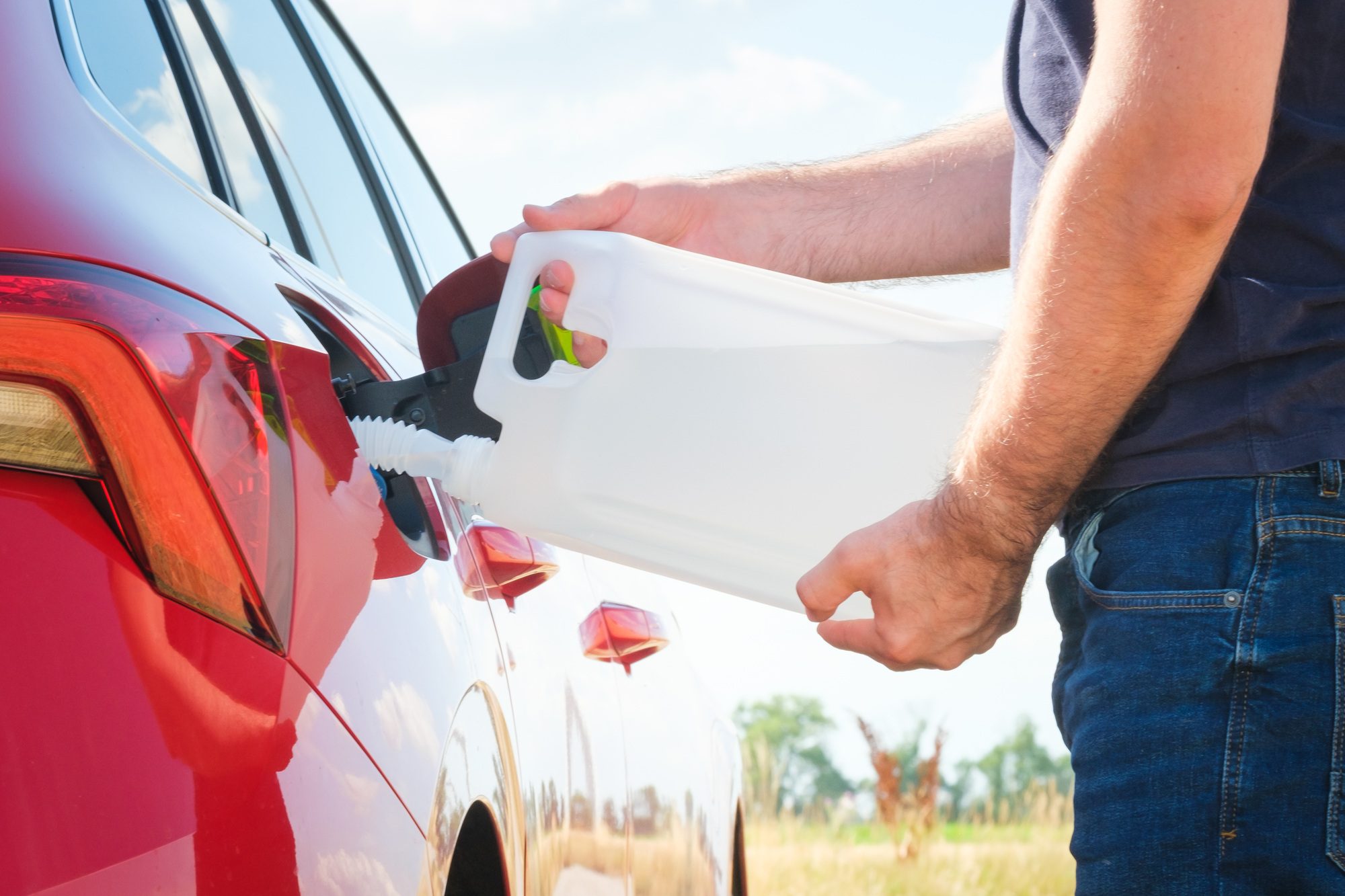 Close up woman refilling the red car with fuel or a diesel engine fluid from canister in the field Close up woman refilling the red car with fuel or a diesel engine fluid from canister in the field