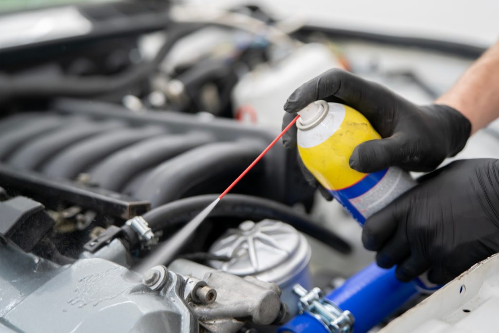 Using a car cleaner spray, a person applies it to engine